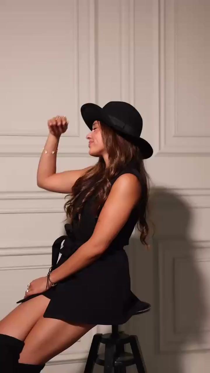 Naomi van Aarle in het zwart met hoed, dansend voor een lichte paneelwand.