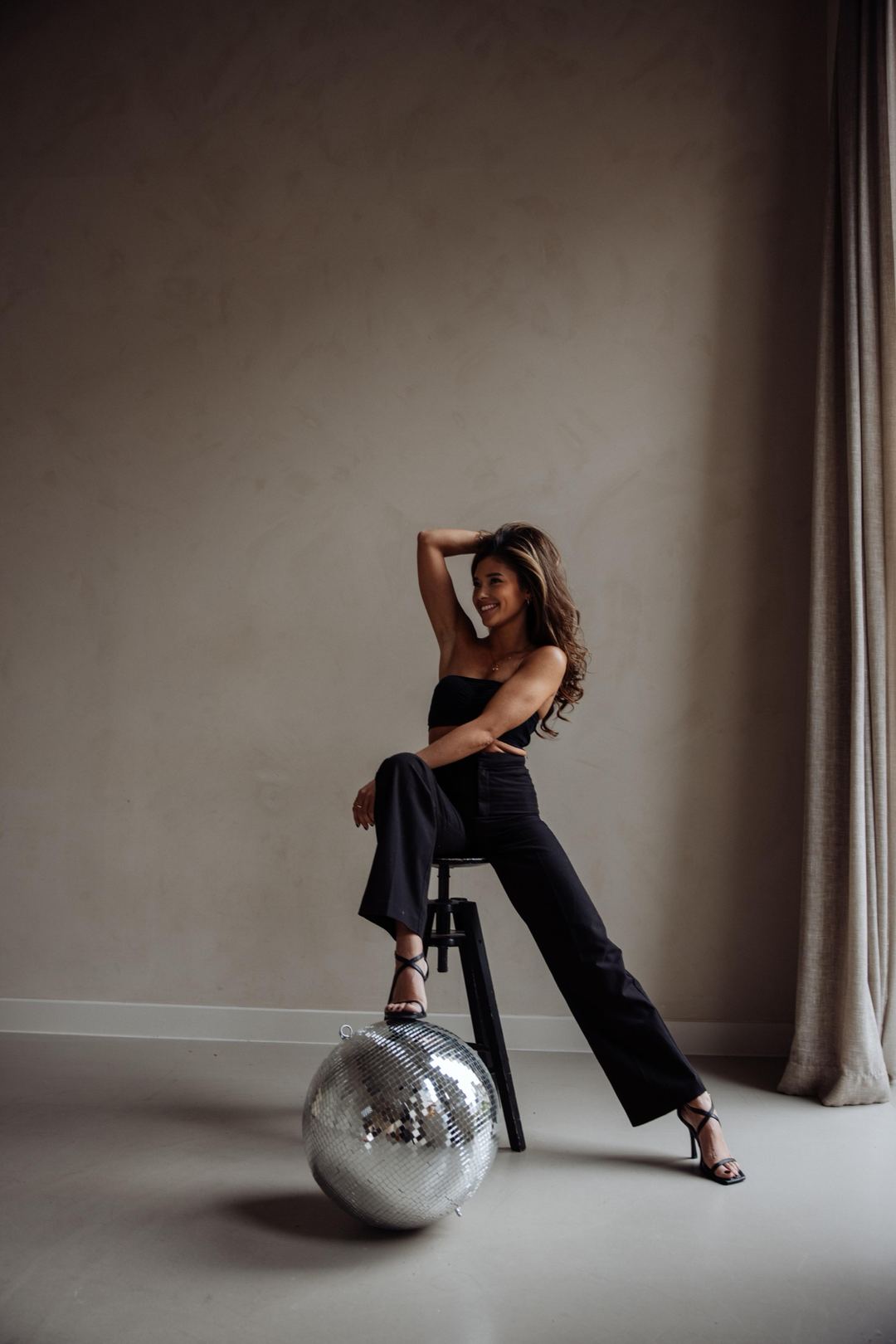 Naomi lachend op een kruk, met een voet op een discobal