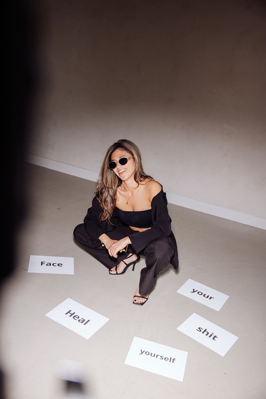 Naomi met zonnebril op de vloer, tussen de woorden Face your shit en Heal yourself.